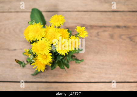 Bouquet von gelben Löwenzahn mit Blättern auf einem alten Holztisch, Ansicht von oben Stockfoto