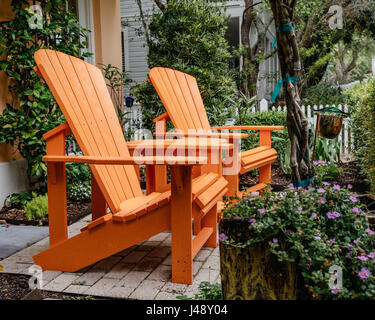 Helles orange Adirondack Liegestühle im Garten im Innenhof in Seaside, Florida USA. Stockfoto