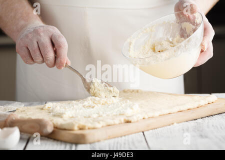 männliche Hand hob geschmolzenen Käse aus Glasschale für Käsekuchen Stockfoto