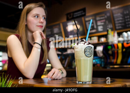 Junge blonde Frau im örtlichen Café am Holztisch Getränk Frappe mit Minze und Schaum Stockfoto