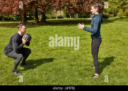 Mann wirft Fitnessball auf Personal Trainer im Park im Sommer Stockfoto