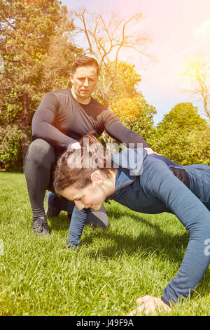 Frau mit Fitness-Trainer macht Push-Ups im Park im Sommer Stockfoto