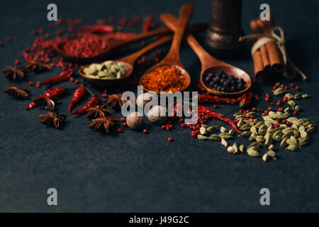 Aromatische Gewürze in Holz Löffel auf dunklen Stein Hintergrund Stockfoto