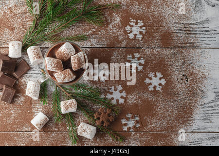 Winter heißer Kakao mit Marshmallows, Schokoladen-Sirup, Zucker Schneeflocken in ein hohes Glas auf einem hölzernen Hintergrund. Stockfoto