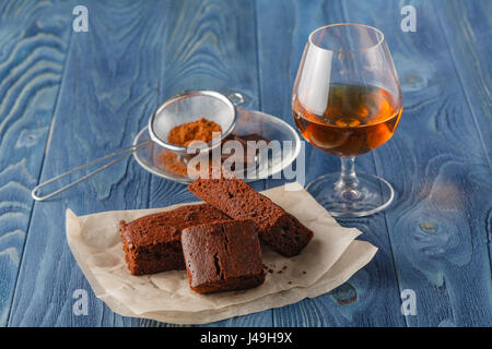 Stapel von drei Stücken Schokolade Brownie Kuchen auf einem hölzernen Hintergrund mit zerknüllten weißen Backpapier. Streuung von Schokolade im Vordergrund Stockfoto