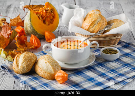 Cremige Kürbis-Suppe mit Kürbiskernen und Creme auf rustikalen Holz Hintergrund mit Herbstlaub gekrönt Stockfoto