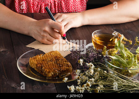 Frau schreiben Rezept Kräutertee. Tasse Kräutertee mit Lindenblüten auf einem alten hölzernen Hintergrund Stockfoto