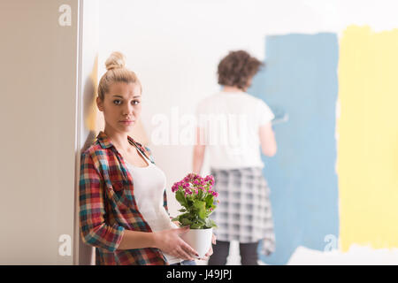 Glückliches Paar Haupterneuerungen zu tun, ist der Mann das Zimmer und die Frau halten den Topf mit Blumen Malerei. Stockfoto