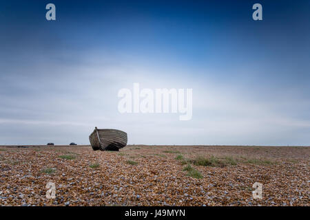 Einsames Fischerboot an einem verlassenen Kiesstrand in Dungeness in Kent, Großbritannien, vor einem blau bewölkten Himmel. Stockfoto