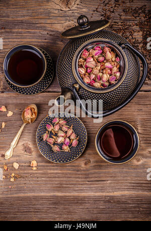 Gusseisen-Tee-Set mit trockenen Rosenknospen auf hölzernen Hintergrund Stockfoto