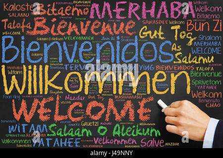 Hand schreibt Willkommen in vielen internationalen Sprachen mit bunter Kreide auf Tafel Stockfoto