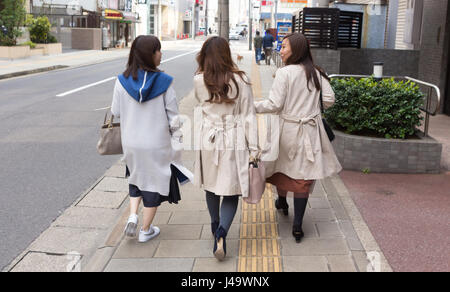 Nagasaki, Japan - März 26., 2017: drei japanischen Mädchen zu Fuß auf dem Bürgersteig, zwei von ihnen tragen Trenchcoat. Stockfoto