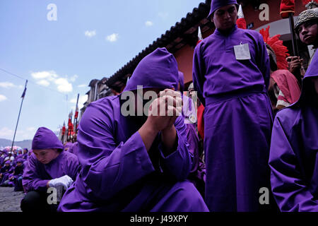 Männer, gekleidet in purpurne Gewänder vor der Anda (Float) das Kreuz Jesu beten Vergehen während der Semana Santa oder Heilige Woche Feier in der Stadt Antigua Guatemala Stockfoto