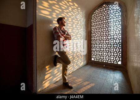 Ein Mann lehnt sich an eine Wand neben dem geometrischen Marmor vergitterten Jali-Bildschirm in Humayun Mausoleum befindet sich in Neu-Delhi, Indien. Stockfoto