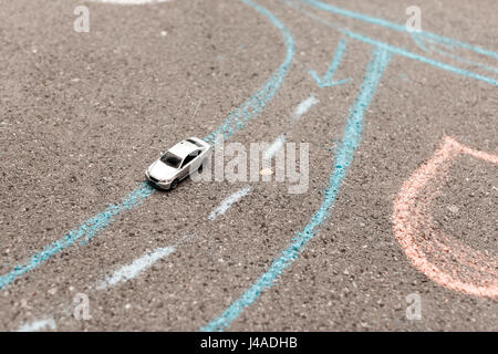 Spielzeugauto auf einem Asphalt. Kreide gemalt Fahrbahnmarkierungen. rechten Bewegung, Drehung und Streifen. Stockfoto