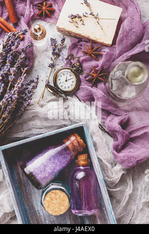 Flasche mit aromatischen Lavendel-Öl und Meersalz in einer Holzkiste, eine Flasche Parfüm, ein Bouquet von Lavendel, Stück Seife und eine Vintage Taschenuhr. Stockfoto