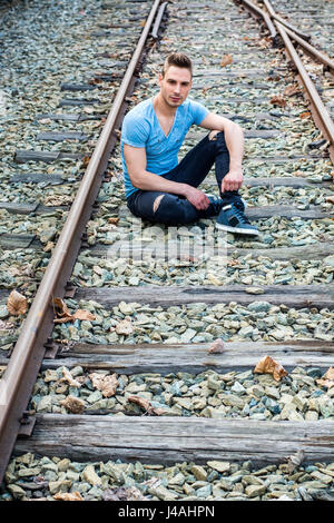 Attraktive junge Mann sitzt auf Eisenbahn Stockfoto