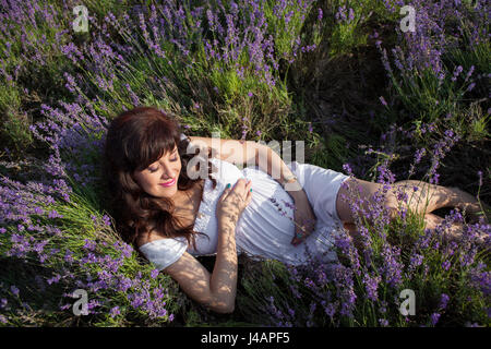 Schwangere Frau liegt in einem Feld von Blumen Stockfoto