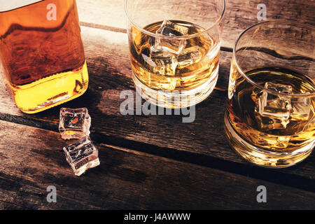 Whisky-Flasche und Gläser mit Eis auf dunklen Holztisch Stockfoto