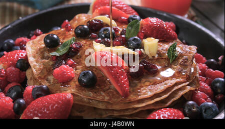 Honig in Strömen über ein Frühstück mit Pfannkuchen mit Beeren und getrockneten Früchten Stockfoto