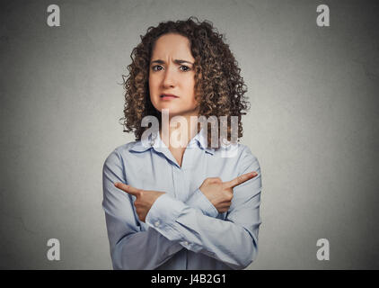 Unentschlossenheit Verwirrung. Porträt verwechselt junge Frau zeigte in zwei verschiedene Richtungen nicht sicher welchen Weg Sie gehen isoliert grau hinterlegt. Negative e Stockfoto