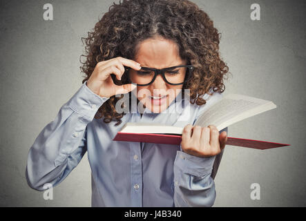 Closeup Portrait junge Frau mit Brille, Buch zu lesen versuchen Schwierigkeiten sehen Text, schlechte Sicht Blick Problem isoliert grau hinterlegt. Stockfoto