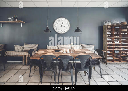 Esstisch in einem Retro-Wohnzimmer mit Möbeln aus Holz und eine große Uhr an der Wand hängen Stockfoto