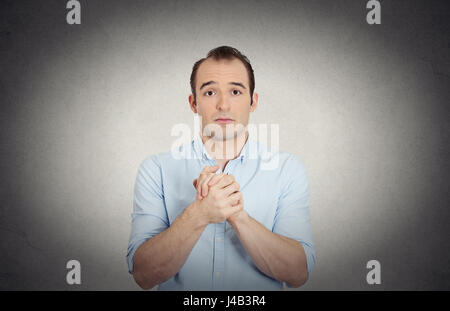 Closeup Portrait verzweifelten junger Mann zeigt gefalteten Händen, bitte schön mit Zucker auf obere isolierte graue Wand Hintergrund. Menschliche Emotionen Gesichts expres Stockfoto