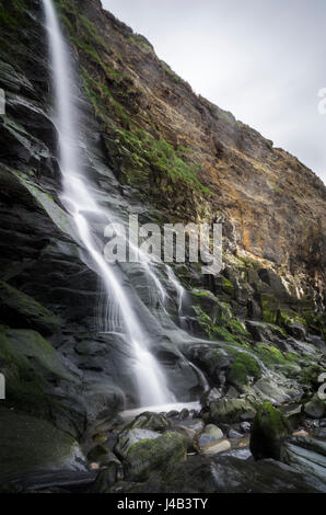 Wasserfall des Flusses spricht fließt über Klippen am Strand an der Tresaith Bucht, einem Küstendorf in Ceredigion, Wales. Stockfoto