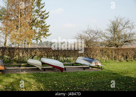 Boote in einer Zeile auf dem Land im Herbst in einem Park mit Rasen und Bäumen in der Nähe von einem See. Stockfoto