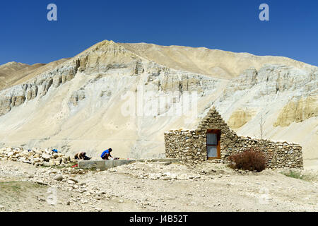 Zwei Loba Männer neben einem Gebäude aus Stein in der Nähe von Tsarang, Upper Mustang, Nepal. Stockfoto