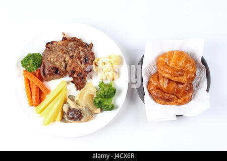 Hausgemachte, Schweinesteak mit in Scheiben geschnittenen Karotten, Pilzen, Mais und Croissants. Stockfoto