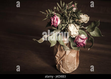 Bouquet von getrockneten roten und weißen Rosen steht auf Holztisch, niedrige Schlüsselfoto Closeup mit selektiver Weichzeichner Stockfoto