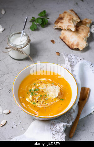 Draufsicht, Schüssel mit Kürbis curry Creme Suppe am Tisch serviert mit Brot und Sauerrahm. Gesunde vegane Ernährung. Stockfoto