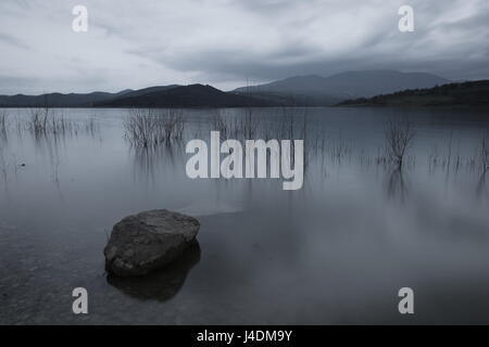 Eine Langzeitbelichtung Foto eines großen Felsens in einen See, unter einem bewölkten Himmel Stockfoto