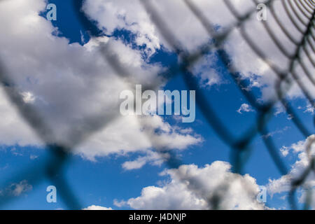 Hintergrund der Metal mesh-Zaun gegen den tiefblauen Himmel mit weißen flauschigen Wolken im Hintergrund. Konzept von Gefängnis und Freiheit. Stockfoto