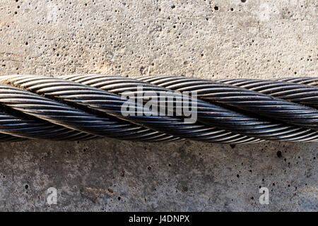 Verdrehte Stahlseil auf einer grauen Betonplatte. Stockfoto