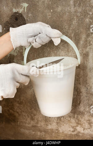 hands of plasterer holding bucket with plaster and spatula on the concrete wall background Stockfoto
