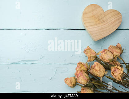 Liebe Feier Hintergrund getrocknete Pfirsich Rosen und aus Holz geschnitzte Herz isoliert auf rustikalen gemalten blauen Tisch Stockfoto