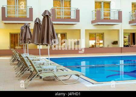 Leere Sonnenliegen und Sonnenschirme sind am Pool leer ohne Touristen in frühen Morgenstunden. Entspannen Sie und Sonnen Sie Pool mit klaren, blauen Wasser im Hotel Resort. Bal Stockfoto