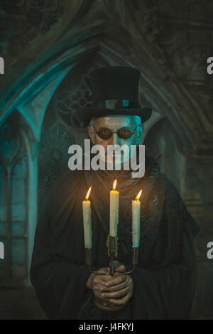 Fremd und beängstigend Mann, stehend mit einem Leuchter, Kerzen brennen. Männer hinter der alten Burg. Stockfoto