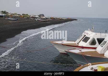 Boote in einem Meer sind mit Seil am Ufer gebunden. Ein Blick auf viele Boote an Land, auf einer Wiese in der Nähe von vulkanischen Sand und welliges Meer auf die Insel Stromboli in Italien. Stockfoto