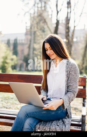 Porträt einer jungen professionellen Frau mit einem Laptopcomputer sitzend auf einer Bank in einem park Stockfoto