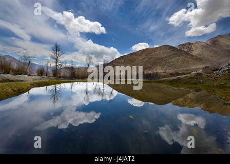 Blauer See zwischen den hohen Bergen: Hänge der Hügel, weiße Wolken und blauer Himmel spiegeln sich in der Oberfläche des Wassers, Frühling im Himalaya, noch Stockfoto