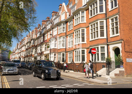 Blick auf Straße mit Menschen zu Fuß, schwarze Kabine und restaurierte elegante edwardianische Luxus-Häuser in roten Ziegeln in der exklusiven Gegend von South Kensington Stockfoto