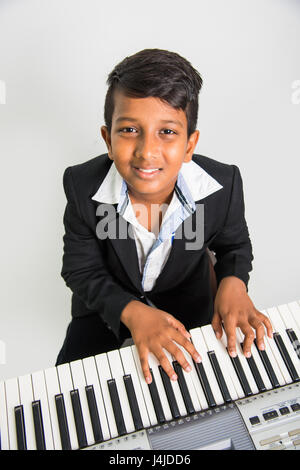 Niedlicher kleiner indischer/asiatischer Junge, der Klavier oder Keyboard spielt, ein Musikinstrument, auf weißem Hintergrund Stockfoto