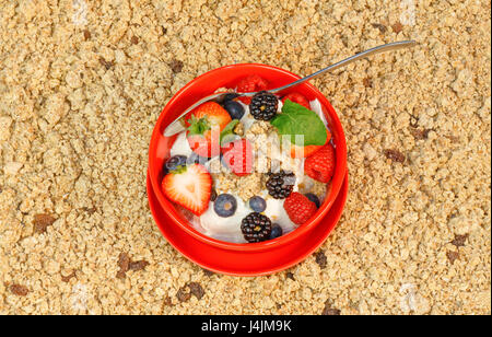 Draufsicht von roten Früchten mit Joghurt und Müsli in einer roten Schüssel Müsli im Hintergrund Stockfoto