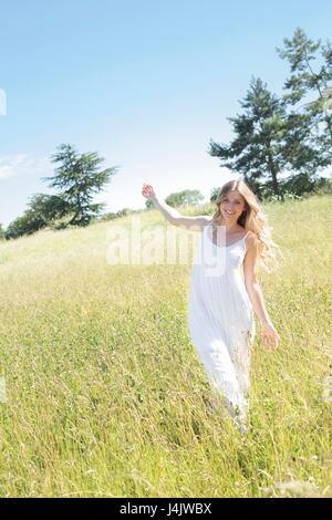 Junge Frau in langen weißen Kleid wandern in der Wiese. Stockfoto