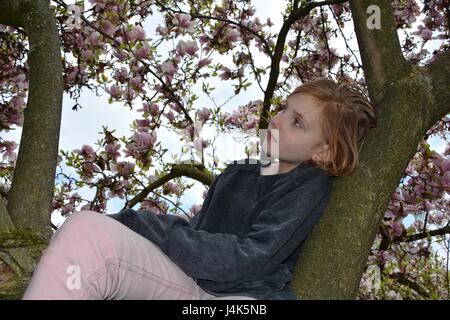 Junges Mädchen sitzt in einem Magnolienbaum und blickt zur Seite Stockfoto