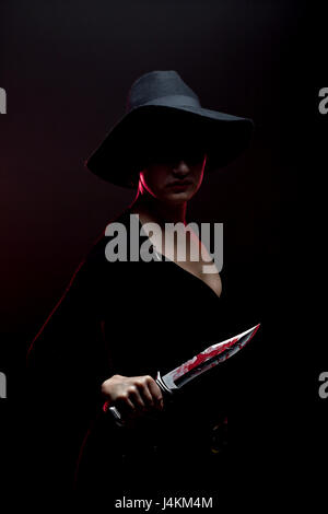 Mädchen mit einem riesigen blutigen Messer im Schatten, Rote Hintergrundbeleuchtung Stockfoto